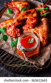 Chicken wings with hot tomato sauce on a chopping board. Grey stone background. Selective focus.  