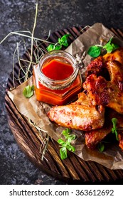 Chicken wings with hot tomato sauce on a chopping board. Grey stone background. Selective focus.