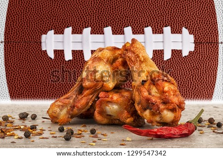 Chicken wings with red hot chili pepper, salt and peppercorn. Football ball image in background.
