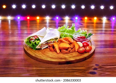 Chicken wrap sandwich with potatoes, vegetables and sauce on a wooden background with lights.