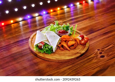 Chicken wrap sandwich with potatoes, vegetables and sauce on a wooden background with lights.