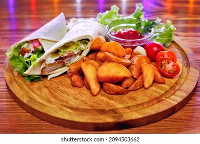 Chicken wrap sandwich with potatoes, vegetables and sauce on a wooden background.