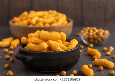 Chickpea cheddar cheese plant based puffs sitting in black ceramic bowl surrounded by toasted chickpeas and an additional bowl of puff in the background