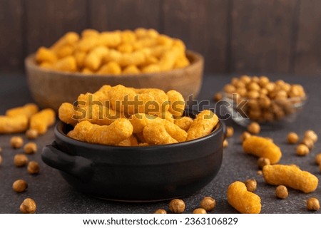 Chickpea cheddar cheese plant based puffs sitting in black ceramic bowl surrounded by toasted chickpeas and an additional bowl of puff in the background