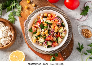 Chickpea salad with tomatoes, cucumber, feta cheese, parsley, onions and lemon in a plate on a gray background top view, selective focus. Healthy vegetarian food, oriental and Mediterranean cuisine. - Shutterstock ID 1677381802