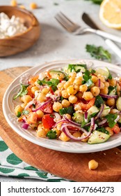 Chickpea salad with tomatoes, cucumber, feta cheese, parsley, onions and lemon in a plate on a served table, selective focus. Tasty and healthy vegetarian food, oriental and Mediterranean cuisine. - Shutterstock ID 1677664273