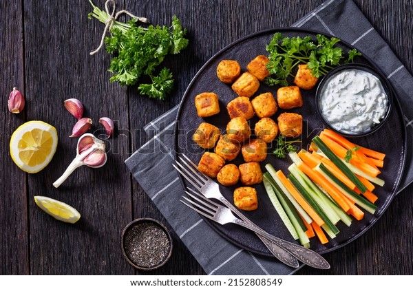 chickpea and veggies mini rolls or gnocchi served\
with fresh cucumber and carrot sticks and yogurt based sauce with\
herbs on black plate on dark oak wood table, horizontal view from\
above, flat lay