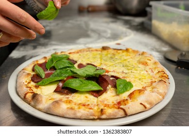 Chief baker adding Fresh basilic Truffle oil and Italian Dry-Cured Beef pizza on a plate ready to be served at a pizzeria.