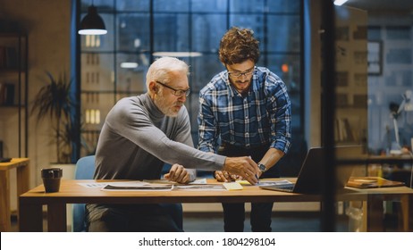 Chief Creative Designer Discusses Design Sheets with Young Developer. Two Professionals Having Discussion, Working with Documents, Choosing Right Concept. Evening in the Stylish Modern Studio Office - Powered by Shutterstock