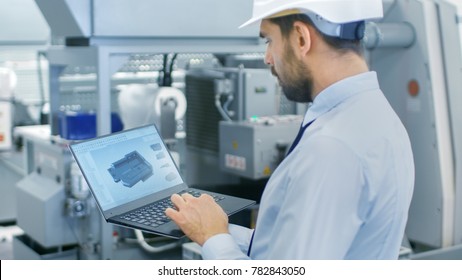 Chief Engineer in the Hard Hat Holds Laptop with 3D Component Model on it's Screen. In the Background Modern Factory Equipment. - Shutterstock ID 782843050