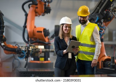 Chief engineer and project manager in modern industrial factory with robot arms talking and planning optimization of production. - Powered by Shutterstock