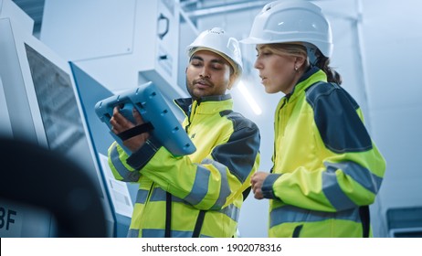 Chief Engineer and Project Manager Wearing Safety Vests and Hard Hats, Use Digital Tablet Controller in Modern Factory, Talking, Programming Machine For Productivity. Low Angle Portraits - Powered by Shutterstock