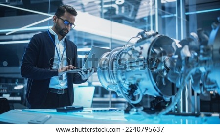 Chief Engineer Using Laptop Computer, Analyzing and Researching How a Futuristic Turbofan Motor Works. Senior Manager Developing Innovative Technology in Industrial High Tech Facility.