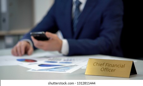 Chief financial officer checking data in annual report, using smartphone, work