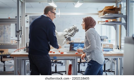 Chief Male Engineer Chatting With Arabic Female Computer Science Specialist While Standing Next To The Table With Robotic Hand. Promising Engineering Majors Collaboration Concept. Medium Shot.