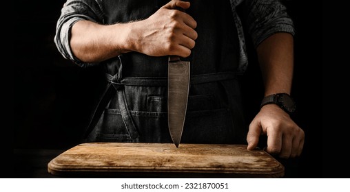 Chief man in apron stubs knife blade to wooden board at kitchen. Restaurant professional with culinary tool - Powered by Shutterstock