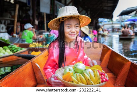 Chikd sit on the boat and hold the fruit basket in Traditional floating market , Thailand.