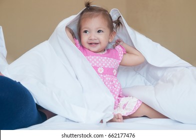 Child 1 Year 2 Months Play Peekaboo With White Blanket Near Her Mom On Bed In Bedroom.