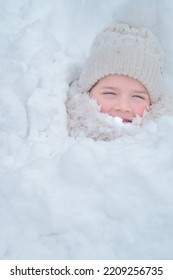 Child, 6 Years Old Boy Laughing And Hiding In The Snow. All Body Covered. Head An Face Only Exposed. Looking To The Camera. Funny Time During Winter Playing In The Snow.