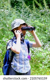 child of 7-8 years, boy in Panama hat, plaid shirt with walkie-talkie in hand stands in forest, looks carefully through binoculars, concept of hiking in nature, tourism, orienteering, survival in wild - Shutterstock ID 2105765159