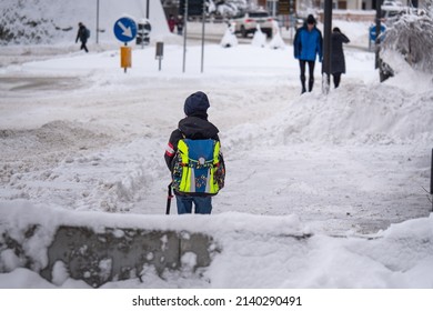 Child About 7 Years Old Walking Down A Snow Covered Street With His School Bag Over His Shoulder On A Cold, Snowy Winter Day.