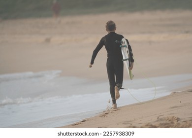 child about to go surfing at the beach, view from behind. - Shutterstock ID 2257938309