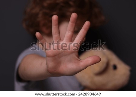 Child abuse. Boy with toy making stop gesture near grey wall, selective focus