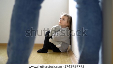 Child abuse concept. Little girl on the floor scared of adult standing.