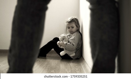 Child abuse concept. Mistreated little girl seating on the floor and scared of adult.