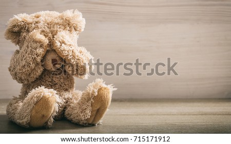 Child abuse concept. Teddy bear covering eyes in an empty room, front view, copy space