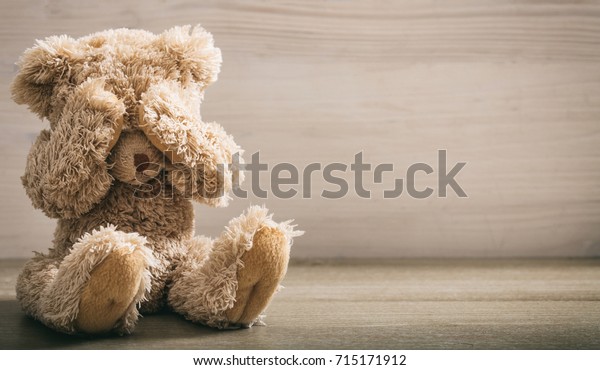 Child abuse concept. Teddy bear covering eyes in an empty room, front view, copy space