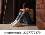 Child abuse. Upset little girl sitting on floor near brick wall indoors