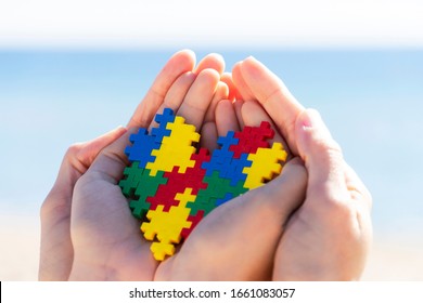 Child And Adult Hands Holding Colorful Heart With Blue Background Outdoors. World Autism Awareness Day Concept