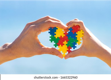 Child And Adult Hands Holding Colorful Heart On Blue Sky Background. World Autism Awareness Day Concept