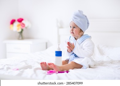 Child After Bath. Cute Little Girl With Wet Curly Hair Wearing A Bathrobe And Head Towel Sitting On A White Bed Using Lotion And Brush. Hygiene For Kids. Bathroom Textile For Babies And Children.