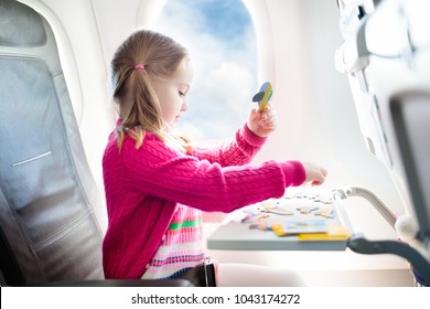 Child In Airplane. Kid In Air Plane Sitting In Window Seat. Flight Entertainment For Kids. Traveling With Young Children. Kids Fly And Travel. Family Summer Vacation. Girl With Toy In Airplane.