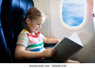 Child In Airplane. Kid With Book In Air Plane Sitting In Window Seat. Flight Entertainment For Kids. Traveling With Young Children. Kids Fly And Travel. Family Vacation. Girl Reading Book In Airplane.