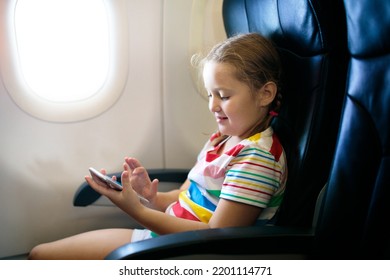 Child In Airplane. Kid With Mobile Phone In Air Plane In Window Seat. Flight Entertainment For Kids. Traveling With Young Children. Kids Fly And Travel. Family Vacation. Girl Playing With Smartphone.