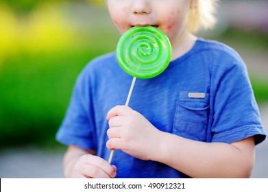 Child With Allergic Reaction Eating Big Green Lollipop. Unhealthy Sweet Food For Young Kids. Allergic Rash Dermatitis On Toddler Skin Face. 