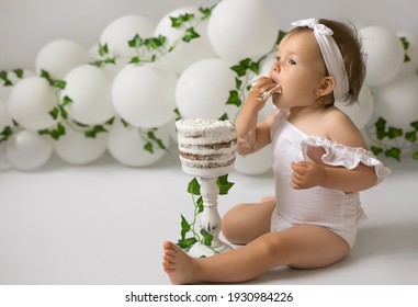 A Child With An Appetite Eats A Birthday Cake For His First Birthday. Festive Decor Made Of Balloons And Trailing Ivy. 