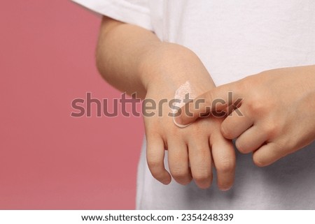 Child applying ointment onto hand against pink background, closeup