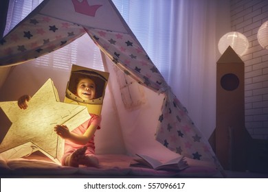 Child in an astronaut costume playing and dreaming of becoming a spacemen. Happy kid plays in tent. Funny lovely girl having fun in children room. 