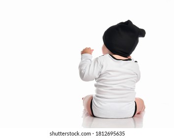 Child Baby Toddler Sitting Facing Backwards From The Back Looking At The Corner Isolated On A White Background. Boy Is Wearing A White Bodysuit And A Black Hat. Place For Text.