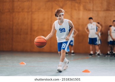 A child in basketball attire is seen practicing ball handling in a basketball sport session in a gymnasium - Powered by Shutterstock