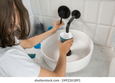 A child in the bathroom in the morning fills a cup with water from the faucet to rinse their mouth and brush their teeth. The boy fills a glass with water. - Powered by Shutterstock