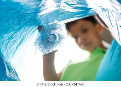 Child Becoming Aware Of The Importance Of Recycling, Places Plastic Bottle In Bag. Separation Of Materials For Recycling.