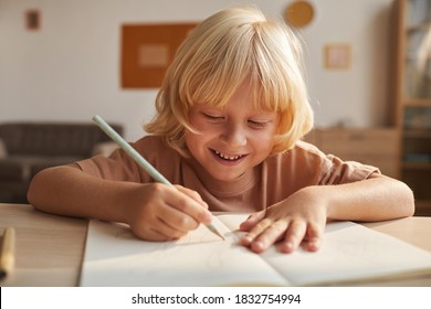 Child With Blond Hair Writing The Report In Note Book He Doing Homework After School