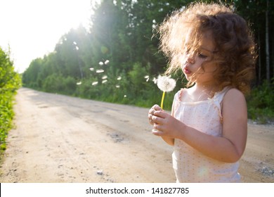 Child Blowing On A Dandelion