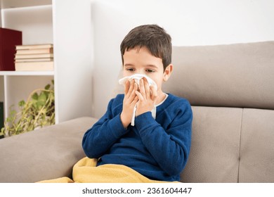 Child blowing in a wipe suffering flu symptoms sitting on a sofa at home in winter - Powered by Shutterstock