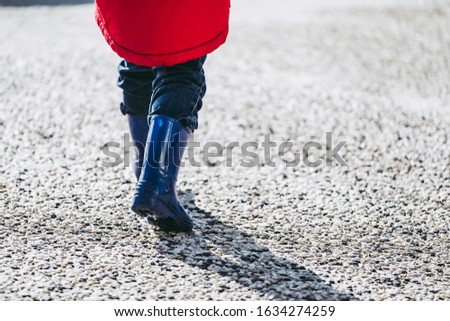 Child with blue rain boots walking on the sand